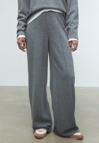 Šedé široké nohavice vyrobené z mäkkej tkaniny, s vertikálnymi švami a voľným strihom, skombinované s svetlými topánkami.