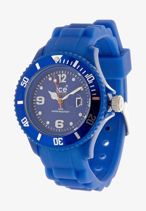 Reloj de silicona azul con una caja redonda y texturizada. Presenta una esfera azul, marcadores de horas blancos, manecillas plateadas y una pantalla de fecha. Resistente al agua.