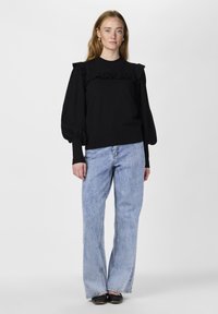 Svart tröja med volangdetaljer vid axlarna och långa puffärmar, i kombination med ljusblå vida jeans och svarta ballerinas.