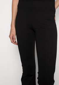 Černé strečové kalhoty vyrobené z měkkého materiálu, s vysokým pasem, vertikálními švy a hladkou, elegantní texturou.