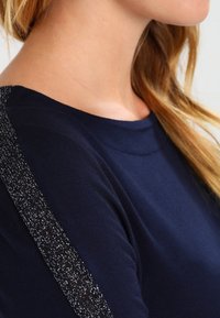 Mörkblå bomullströja med rund halsringning och glittriga detaljer på axlarna. Mjuk textur med en kroppsnära passform.