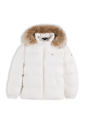Pige smilende, iført en hvid dunjakke med pels-hoodie, stribet sweater, blå viddejeans og sorte sko, stående mod hvid baggrund.
