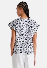 Blusa de estampado floral en blanco y azul marino, con mangas cortas y anchas y un corte relajado. El diseño presenta delicados detalles de flores y hojas.