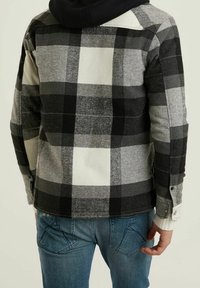 Kraciasta kurtka w kolorach czarnym, szarym i białym o miękkiej fakturze. Posiada czarny kaptur oraz mankiety zapinane na guziki i dwie kieszenie na piersi.