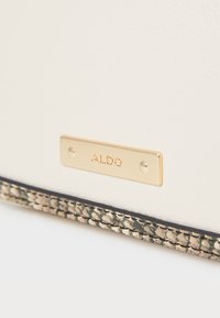 Biele umelé kožené taška s zlatou značkou ALDO. Obsahuje tkanecký detail na spodnej časti v neutrálnej farbe. Hladká textura po celom povrchu.
