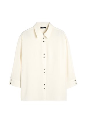 Kremowa koszula z wyłogami, rękawami o długości trzech czwartych i czarnymi guzikami z przodu oraz na mankietach. Gładka faktura materiału.