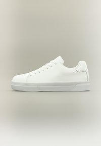 Λευκό sneaker χαμηλού προφίλ με κορδόνια, απαλό δερμάτινο επάνω μέρος και καουτσούκ σόλα πάνω σε απλό ουδέτερο φόντο.