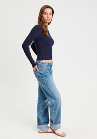 Granatowy prążkowany crop top z długim rękawem w połączeniu z jasnoniebieskimi szerokimi spodniami, które mają wysoki stan i luźny krój. Model ma na sobie buty z różowymi akcentami.