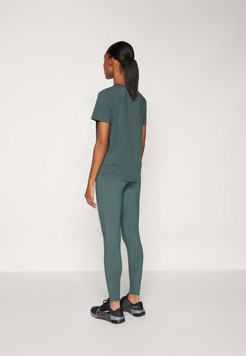 Haut de sport vert foncé et leggings assortis, en tissu flexible, design ajusté, associés à des chaussures de sport noires, vus de dos.