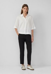 Wit linnen overhemd met knopen, een kraag, korte mouwen en een relaxte pasvorm, gecombineerd met zwarte broek en beige sneakers.
