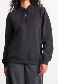 Felpa nera con cappuccio regolabile con coulisse, realizzata in un leggero misto cotone, piccolo logo Adidas bianco sul petto. Tessuto morbido, vestibilità casual.