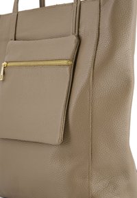 Beige leren tote bag met een gestructureerd oppervlak, voorzien van een voorzak met rits en gouden hardware, en dubbele handvatten aan de bovenkant.