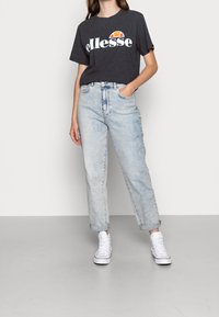 Gray short-sleeve t-shirt with white "ellesse" logo, paired with light blue high-waisted jeans and white sneakers. Casual fit with rolled cuffs.