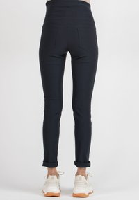 High-waisted navy leggings featuring a smooth, stretchy fabric, slim fit, and two back pockets. Rolled cuffs above white athletic shoes.