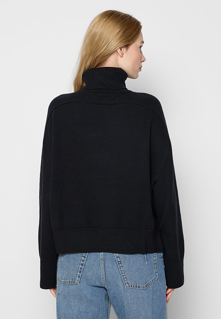 Czarny, krótki sweter z wysokim kołnierzem, z prążkowanymi detalami i miękką teksturą, zestawiony z jasnoniebieskimi dżinsami o wysokim stanie.