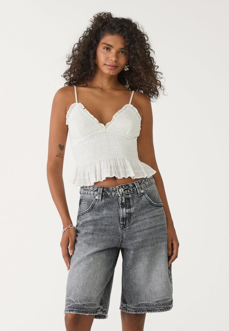 Top court blanchi à smocks avec des bords à volants, associé à un short en denim noir délavé taille haute, doté de poches avant et d'une coupe décontractée.
