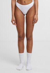Bijele bikini gaćice s višim krojem, uparen s bijelim čarapama do članaka koje imaju suptilno rebraste detalje. Glatka tekstura tkanine.
