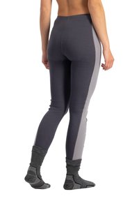 Frau von hinten, trägt dunkelgraue Leggings mit hellgrauen Seitenpaneelen und graue Sportsocken, steht vor einem weißen Hintergrund.