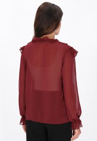 Burgundi selyem chiffon blúz fodrokkal a galléron és a mandzsettákon, puha tapintású, könnyű, félig átlátszó kialakítással.