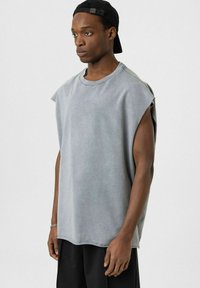 Grijze oversized mouwloze t-shirt van zacht materiaal, met een ronde halslijn en verlaagde armsgaten, gecombineerd met losse zwarte broeken.