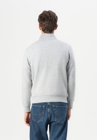 Grå sweatshirt med høj krave og ribstrikkede manchetter, der har en blød tekstur. Sammen med blå jeans med klassisk pasform og baglommer.