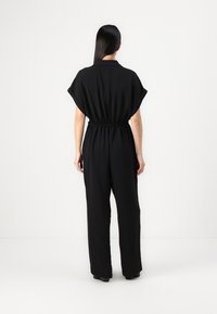 Svart jumpsuit med korte ermer, innsnevret midje og brede ben. Glatt tekstur med en avslappet passform og uten synlige mønstre eller detaljer.