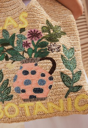 Sac au crochet avec vase à pois brodé tenant des fleurs roses et blanches et des feuilles vertes, texte jaune indiquant "BOTANIC."