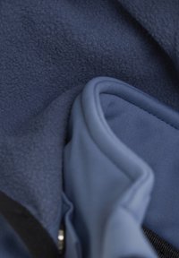 Marintröja av fleece och släta tygskikt, som visar en mjuk textur med en lätt rynkad framtoning nära dragkedjan och kanterna.