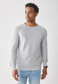 Suéter gris con textura, con un cuello redondo acanalado y mangas largas, combinado con jeans de color azul claro. Diseño sencillo, sin logotipos ni patrones visibles.