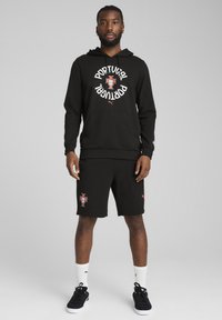 Sort hættetrøje med "Portugal" tekst og logo, sammen med sorte shorts med et Portugal våbenskjold. Sokkene er hvide med et mærke logo.