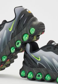 Ténis de corrida Nike com um cabedal em gradiente cinza, detalhes pretos e uma amortização em bolha verde proeminente na sola.