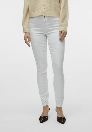 Hvide skinny jeans med fem lommer, lukning med knap foran og en glat stofstruktur. Kombinationen med en lysebrun strikcardigan og mørke flade sko.