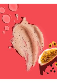 Passionsfrugt halvdel med kerner ved siden af en tekstureret lyserød creme eller scrub med sorte prikker og flere gennemsigtige væskedråber på en rød baggrund.