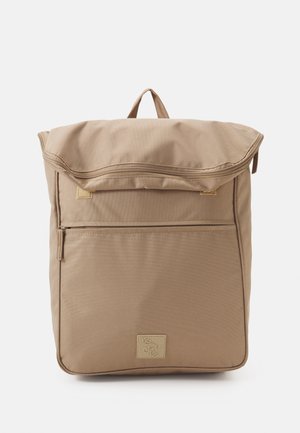 Sac à dos en tissu marron avec un rabat supérieur, une poche zippée à l'avant et un patch logo. Il présente un design plat avec des lignes épurées et une surface texturée.