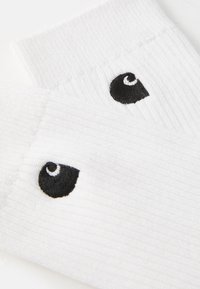 Chaussettes blanches en tissu ribbed avec deux logos noirs brodés. Présentent une bande de cheville rembourrée et une texture lisse.