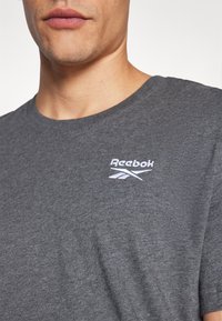 T-shirt in cotone grigio heather con colletto rotondo e maniche corte, con un logo Reebok bianco ricamato sulla parte sinistra del petto.
