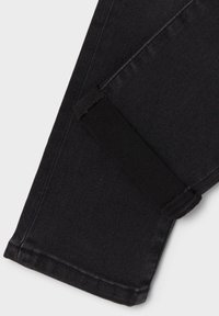 Jeans in denim nero con finitura testurizzata, design a gamba aderente e dettaglio in tessuto nero vicino alla caviglia.