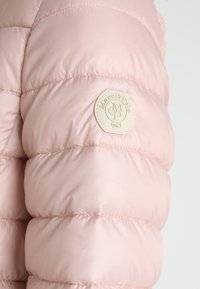 Lys pink, quiltet jakkeærme med en rund beige lap, der har "Marc O'Polo 1967" logoet broderet på.