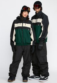 Skisæt i yderbeklædning med et grønt, sort og cremefarvet blokdesign, tekstureret stof, elastiske manchetter, cargobukser og handsker.