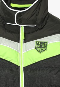 Svart puffjacka med neongrön och grå detaljer. Har en funnel neck, en grön dragkedja och en patch med "CA-RS 19NYC82" på bröstet.