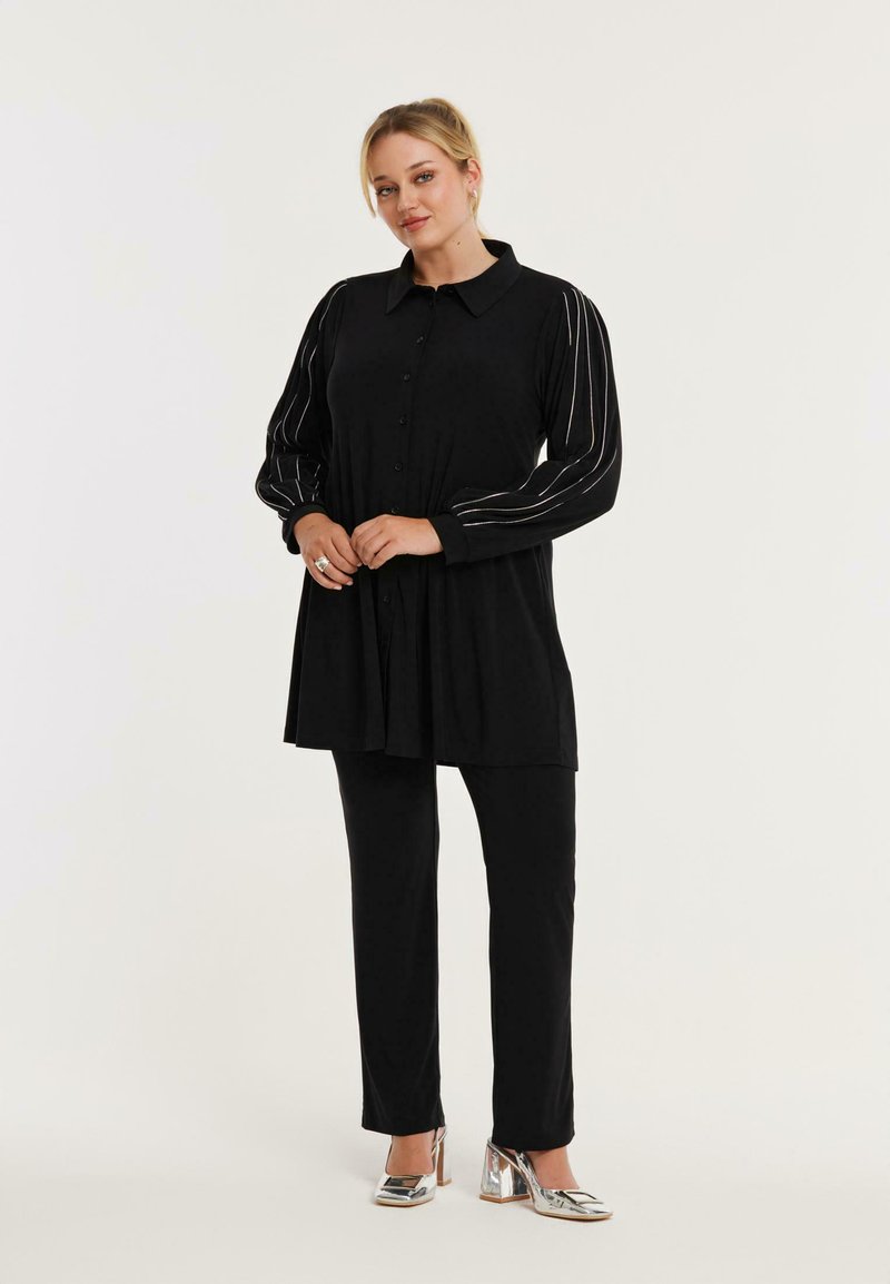 Zwarte blouse met lange mouwen en zilveren strepen, gecombineerd met zwarte broeken en metallic hakken. Soepele stof.