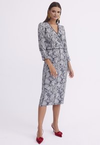 Sukienka w czarno-białym wzorze węża z długimi rękawami, dekoltem w serek i dopasowaną sylwetką. Uzupełniona czerwonymi szpilkami ozdobionymi kokardą.