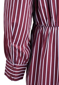 Burgundowa sukienka z pionowymi białymi paskami, długimi bufkami, elastyczną talią i zapiętymi mankietami. Gładka tekstura materiału.