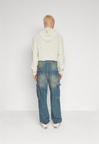 Ljust grå ribbad hoodie med dragsko och blå vida cargoj jeans med fram- och bakfickor samt en blekt finish.