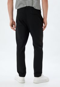 Sorte joggerbukser med elastik i taljen og to baglommer, med en tapered ben design og ribstrikkede manchetter, parret med hvide sneakers.