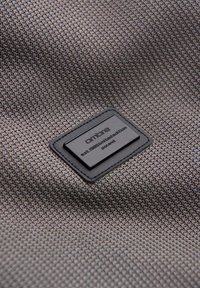 Gros plan sur un tissu gris texturé avec un patch rectangulaire noir portant l'inscription "ombre est. 1985 édition limitée Pologne."