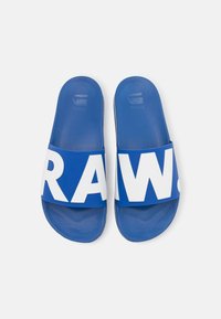 Blue slide sandals with a wide white strap featuring the text "RAW." Textured insole, flat sole design, and a smooth finish.