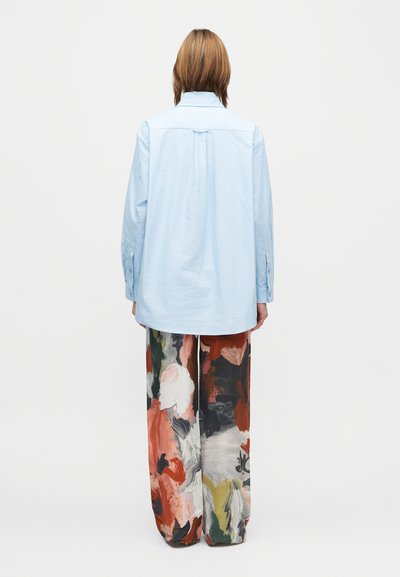 Cămașă supradimensionată de culoare albastru deschis, cu manșete cu nasturi, asortată cu pantaloni cu picioare largi, având un imprimeu floral abstract colorat.