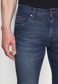 Tmavě modré džíny se slim fit střihem, které mají na přední kapse červenobílý pruhovaný akcent a viditelné švy.