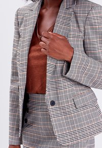 Gestructureerde blazer in zwart, wit en bruine tinten met een getailleerde pasvorm, voorzien van notch revers en een knoopsluiting, gedragen met een bruine top.